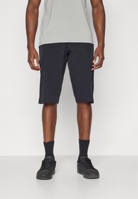 Shorts de sport noirs avec des détails perforés, fabriqués en tissu léger. Associés à un t-shirt gris clair et des baskets noires.