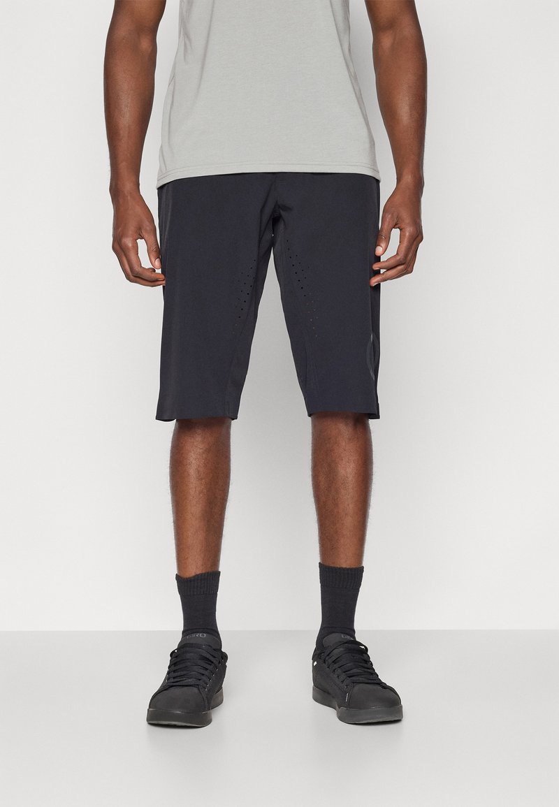 Shorts de sport noirs avec des détails perforés, fabriqués en tissu léger. Associés à un t-shirt gris clair et des baskets noires.