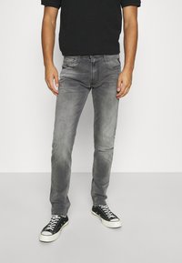 Los jeans de denim gris presentan un ajuste slim, un ligero efecto desgastado y un diseño clásico de cinco bolsillos, combinados con zapatillas de lona negras.