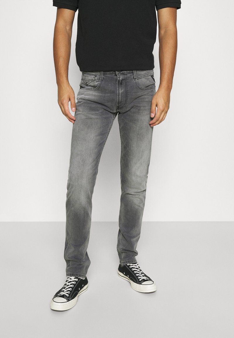 Los jeans de denim gris presentan un ajuste slim, un ligero efecto desgastado y un diseño clásico de cinco bolsillos, combinados con zapatillas de lona negras.