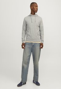 Gray hooded sweatshirt with drawstrings, worn over a beige shirt, paired with light blue baggy jeans and navy sneakers with white stripes.