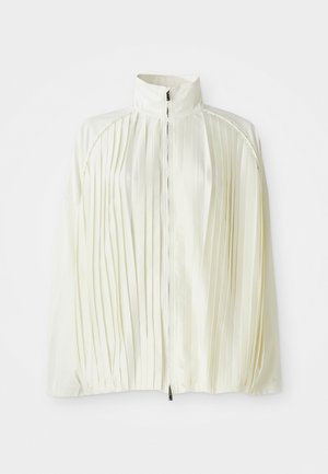 Chaqueta blanca con pliegues, cuello alto, cierre frontal con cremallera y dobladillo elástico. Hecha de una tela ligera y brillante.