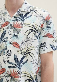 Short-sleeve, button-up shirt featuring a light background with vibrant tropical leaf patterns in green, red, and blue. Smooth fabric.