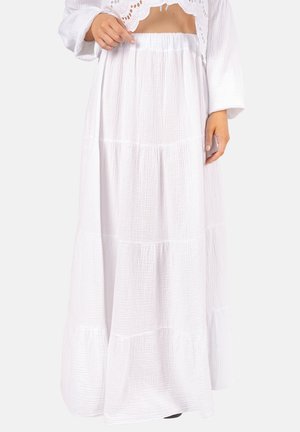 Frau trägt einen langen, weißen, gestuften Rock mit elastischem Bund und strukturiertem Stoff, kombiniert mit einem weißen, kurzen Eyelet-Spitzenoberteil.