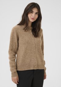 Hnědý kardigan vyrobený z měkké látky, který má kulatý výstřih, dlouhé rukávy a šest knoflíků na přední straně.