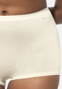 Hochgeschnittene beige Unterwäsche aus weichem Stoff; mit einem gewellten Bund und einem kleinen Markenetikett auf der Vorderseite.