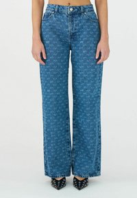 Helleblaue Denim-Jeans mit weitem Bein, subtilem Texturmuster, hoher Taille, Gürtelschlaufen und vorderen Taschen. Dazu werden spitze schwarze Schuhe getragen.