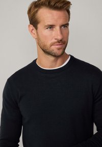 Ciemnoniebieski sweter dzianinowy z okrągłym dekoltem. Gładka faktura, długie rękawy, z białym detalem wewnętrznego kołnierza.