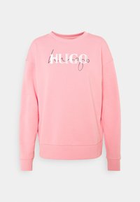 Sweat-shirt rose à manches longues avec col rond, inscription "HUGO" en blanc et noir sur le devant, poignets et taille côtelés.