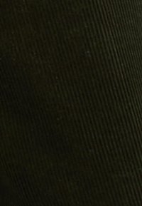 Σκούρο πράσινο βελούδινο ύφασμα με έντονες κάθετες ραβδώσεις. Η επιφάνεια φαίνεται υφασμένη με ομοιόμορφα τοποθετημένες κορυφές και μια απαλή γυαλάδα.