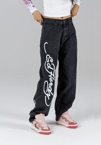 Jeans neri baggy con scritte bianche "Ed Hardy", design a cinque tasche e taglio dritto. Indossati con sneaker alte rosa con un grafico.