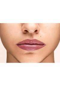 Pomadka w stonowanym odcieniu mauve, gładka tekstura, na pełnych wargach z wyraźnym konturem. Skóra ma naturalne wykończenie, oświetlenie jest miękkie.