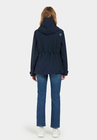 Mörkblå vattentät jacka med åtdragen midja, huva och elastiska detaljer. Tillsammans med ljusblå jeans och vita sneakers.