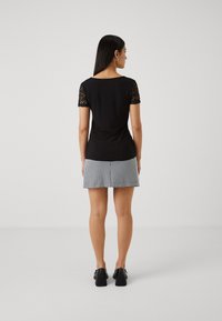 Čierny top s krátkym rukávom a čipkovými detailmi, skombinovaný s sukňou v károvanom vzore. Model má na sebe čiernu obuv. Hladké biele pozadie.