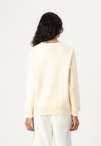 Lys gul sweatshirt med rund hals, lange ermer og ribbestrikkede mansjetter. Myk stoff med minimalistisk design, brukt sammen med hvite jeans.