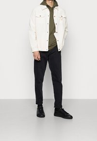 White corduroy jacket, olive green hooded sweatshirt, black jeans, and black sneakers. Features button closure and front pockets.