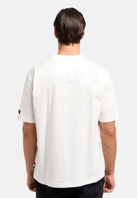 Witte katoenen t-shirt, korte mouwen, met een reliëfopdruk "Milano 1978" op de achterkant en een klein gekleurd label aan de onderrand.
