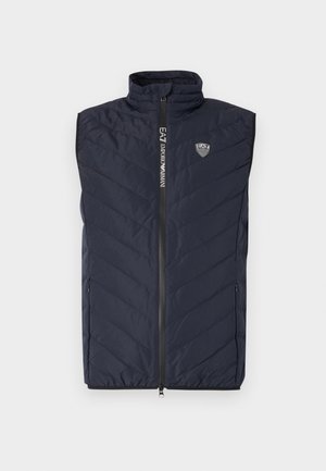 Marineblå uten ermer puffervest med vertikalt kviltet mønster, høy krage, lang glidelås og logo på brystet.