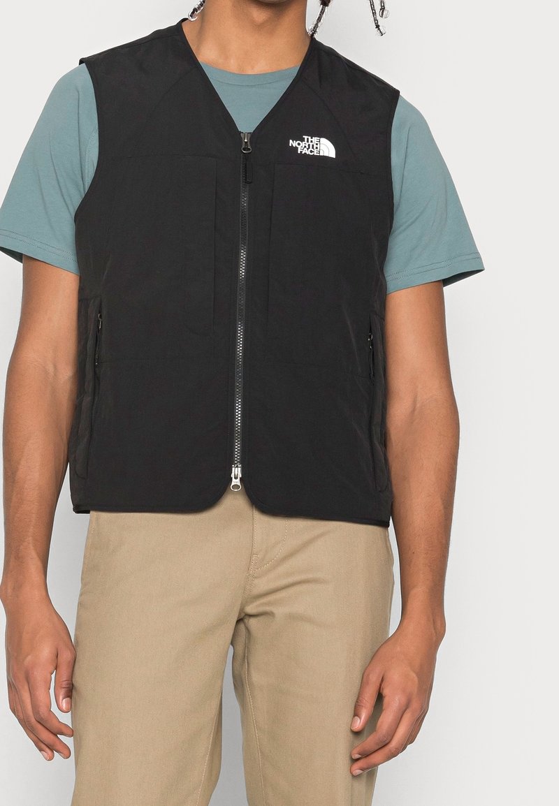 Czarna kamizelka z zamkiem błyskawicznym i dwoma przednimi kieszeniami. Wykonana z lekkiego materiału, posiada białe logo The North Face na klatce piersiowej.