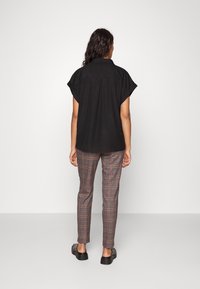 Czarna koszula z krótkim rękawem i kołnierzykiem, zestawiona z szarymi, czerwonymi i zielonymi spodniami w kratę oraz czarnymi butami wsuwanymi. Jednolity tło.