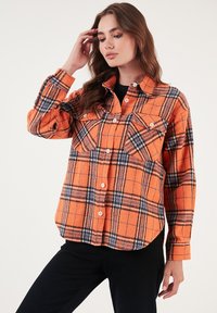 Narancssárga kockás flanel ing, fekete és kék vonalakkal, elöl gombos záródás, két mellzseb és hosszú ujjak. Puha tapintás.
