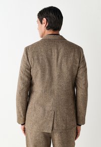Veste de costume en tweed marron avec une coupe cintrée, une fente simple et des revers crantés. Tissu texturé avec un motif de tissage sophistiqué.