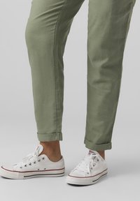 Ljusgröna byxor med uppvikta fållar, tillsammans med vita kanvas sneakers med röda accenter och flera hål.