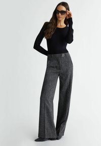 Maglietta nera a costine con maniche lunghe abbinata a pantaloni grigi in tweed a gamba larga con dettaglio zipper in vita, indossata con occhiali da sole neri oversize.