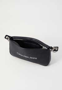 Fekete sima bőrből készült táska, tetején cipzárral záródik, ezüstszínű fémrészekkel, az elején pedig domború "Calvin Klein Jeans" logóval.