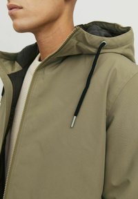 Veste à capuche kaki avec fermeture à glissière, dotée d'un cordon de serrage noir, texture lisse et doublure intérieure contrastante.
