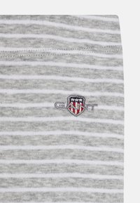 Grå og hvit stripete stoff med en myk tekstur, med en liten GANT-logo brodert i fargene rød, blå og hvit.