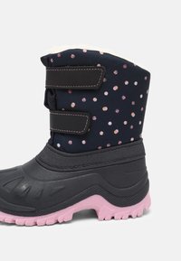 Botte d'hiver pour enfants avec partie inférieure en caoutchouc noir, partie supérieure en tissu bleu marine à pois roses et blancs, deux sangles Velcro noires et semelle extérieure rose.