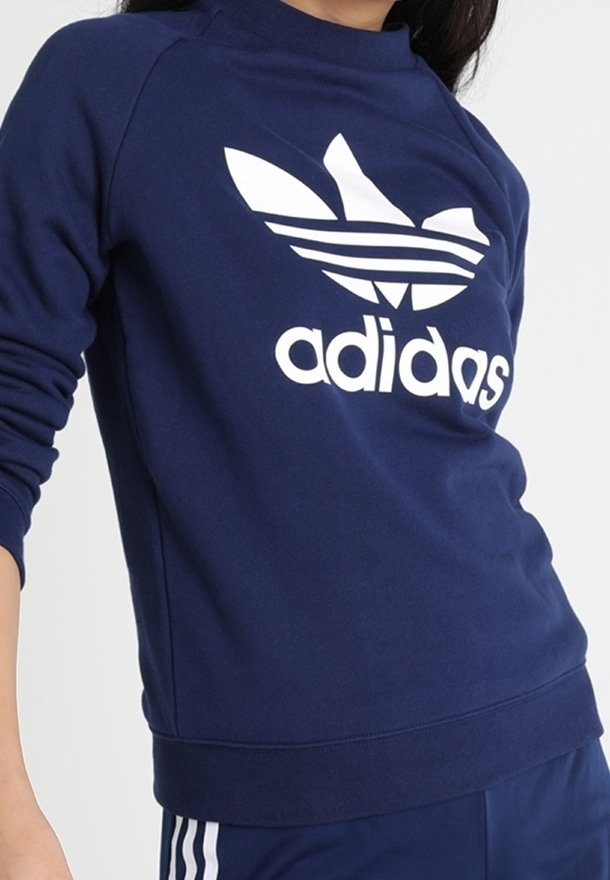Sweatshirt bleu marine en matériau doux, avec un grand logo Adidas trèfle blanc et des poignets et un ourlet côtelés.