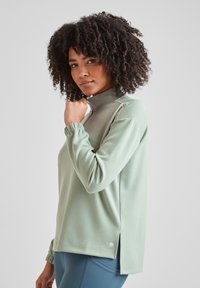 Mint green pullover with a high collar, half zip, and gathered cuffs. Features slits on the sides and logo accent at the hem. Smooth texture.