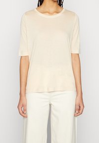 Beżowa koszulka z krótkim rękawem o okrągłym dekolcie, wykonana z lekkiego materiału, charakteryzująca się luźnym krojem i gładką fakturą.