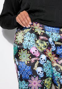 Leggings colorati e fantasiosi realizzati in tessuto liscio. Presentano motivi floreali, teschi e disegni animali in tonalità neon su uno sfondo nero.