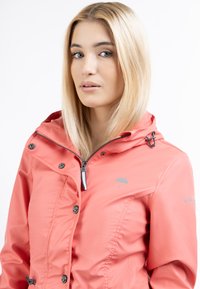 Jachetă impermeabilă coral cu fermoar în față, glugă reglabilă și nasturi tip capse. Dispune de un logo și o textură netedă, lucioasă.