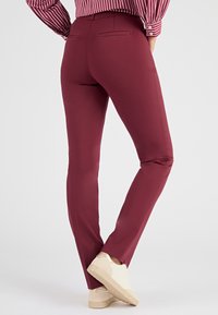 Pantalones ajustados burdeos con una textura suave, que cuentan con dos bolsillos traseros, combinados con zapatillas de color claro y una camiseta a rayas.
