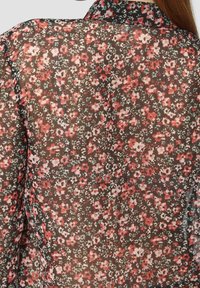 Blouse florale en tissu noir transparent, ornée d'un motif de petites fleurs rouges, roses et vertes, avec un design de col classique.