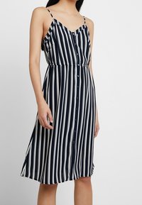 Abito estivo a righe blu navy e bianche con spalline sottili, chiusura con bottoni sul davanti e vita aderente, che si allarga all'orlo per una vestibilità rilassata.
