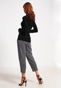 Zwarte blouse met lange mouwen en een gestructureerd patroon, gecombineerd met grijze geruite cropped broek en zwarte sandaaltjes met hoge hakken.