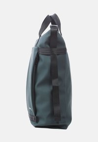 Waterdichte duffelbag in donkerteal met zwarte banden. Beschikt over een zijrits en heeft een ronde vorm, gemaakt van duurzaam, gestructureerd materiaal.