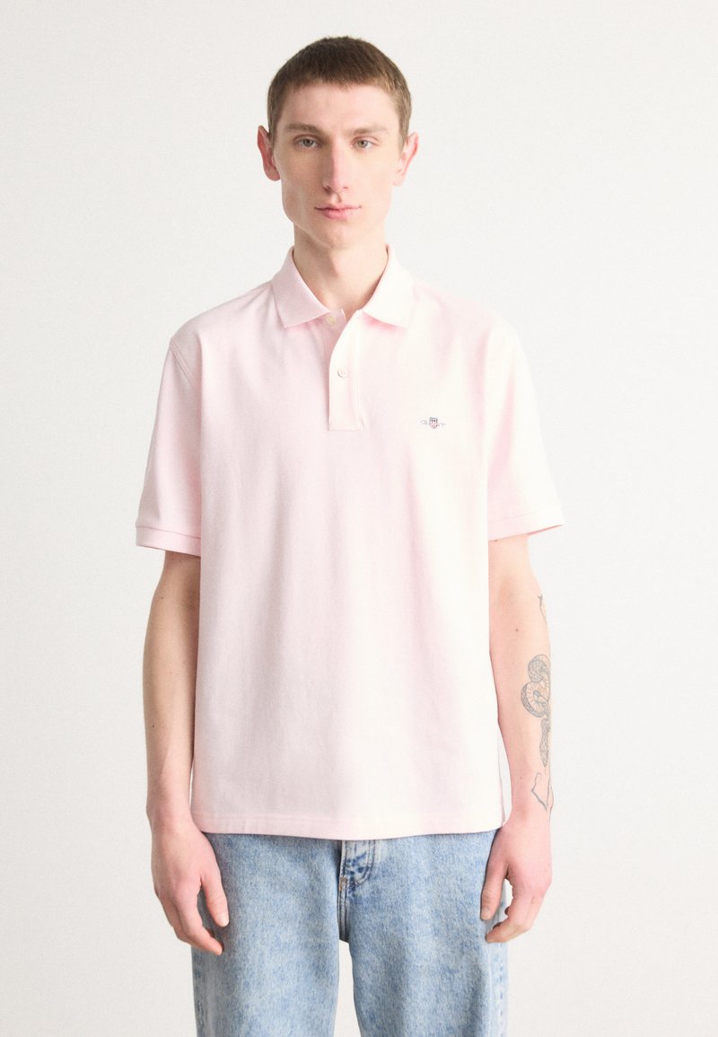 Polo en coton rose clair avec un col classique, des manches courtes et un petit logo brodé sur la poitrine. Porté avec un jean bleu.