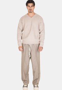 Maglione beige a costine con scollo a V. Pantaloni larghi grigio chiaro con coulisse e finitura testurizzata. Sneakers bianche completano l'outfit.
