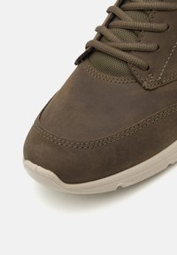 Brown leather sneaker with textured upper, mesh accents, and tonal stitching. Lightweight rubber sole with rounded toe and slight heel.