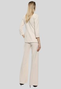 Completo in crema composto da giacca su misura con maniche a tre quarti e pantaloni a zampa, realizzato in tessuto morbido con un design senza cuciture.