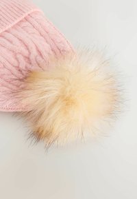 Roze gebreide muts met kabelbrei-design, voorzien van een fluffy nepbont pompon in lichtbeige, die textuur en detail benadrukt.