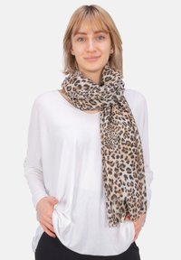 Écharpe en imprimé léopard beige et noir, fabriquée en tissu léger. Portée en drapé, avec une texture douce et des bordures légèrement effilées.