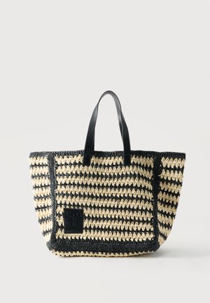 Sort og beige flettet mulepose med sorte læderhåndtag og en sort lap med præget tekst på forsiden nederst til venstre.