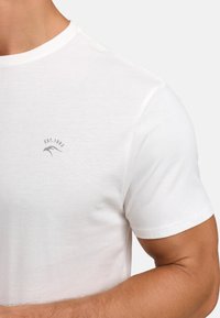 Short-sleeve white cotton t-shirt featuring a crew neck and a small gray logo with "EST. 1983" on the left chest area. Smooth texture.
